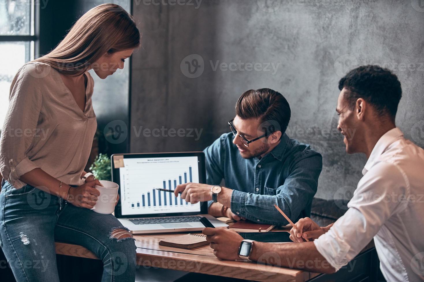Group of young modern people in smart casual wear analyzing data on photo