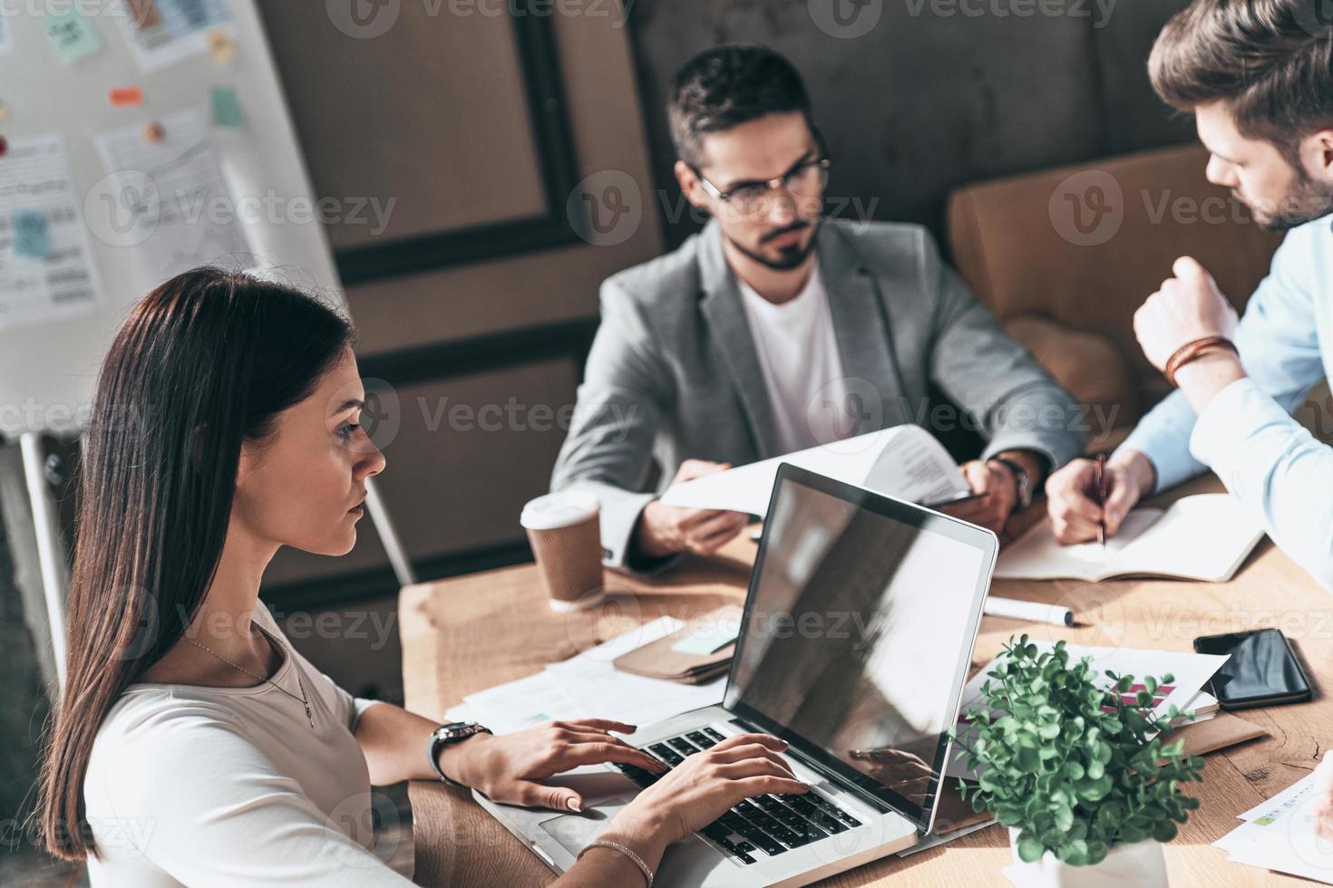 Just working day. Top view of young modern people in smart casual wear discussing business while sitting in the creative office photo