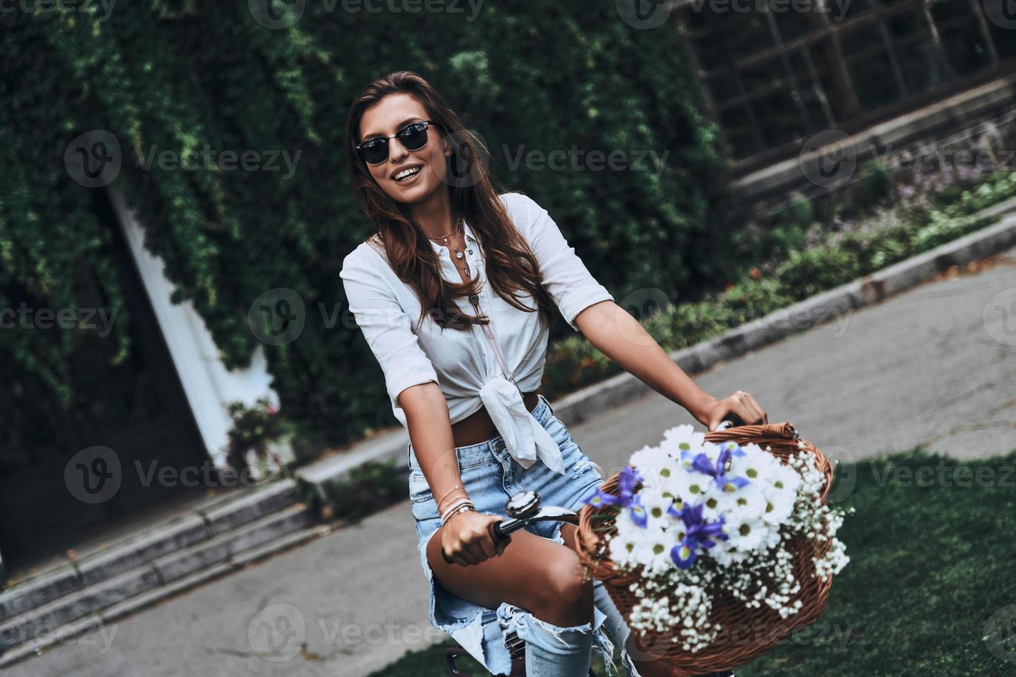 Carefree wheeling. Attractive young woman in casual wear smiling while cycling outdoors photo