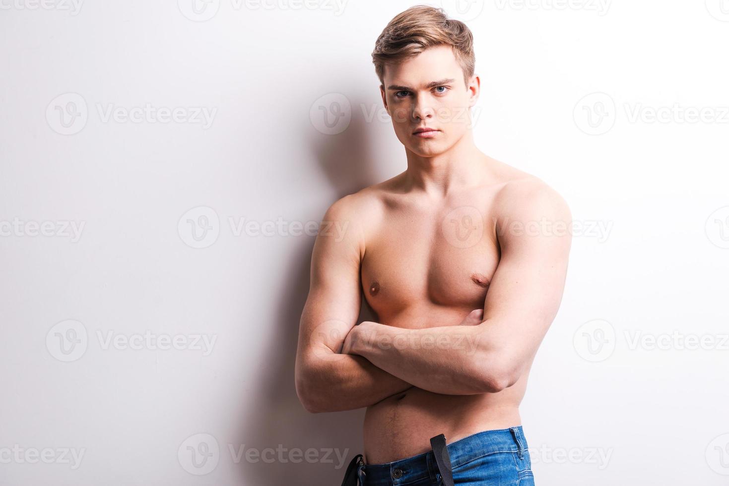 Young and handsome. Handsome young muscular man keeping arms crossed while standing against grey background photo