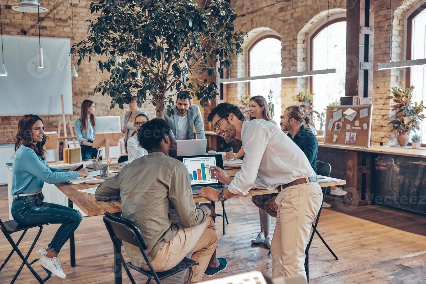 Group of young modern people in smart casual wear communicating and using modern technologies while working in the office photo