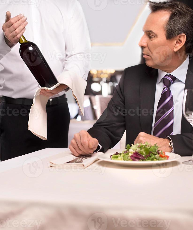 Choosing wine. Sommelier proposing wine to senior man sitting at the restaurant photo