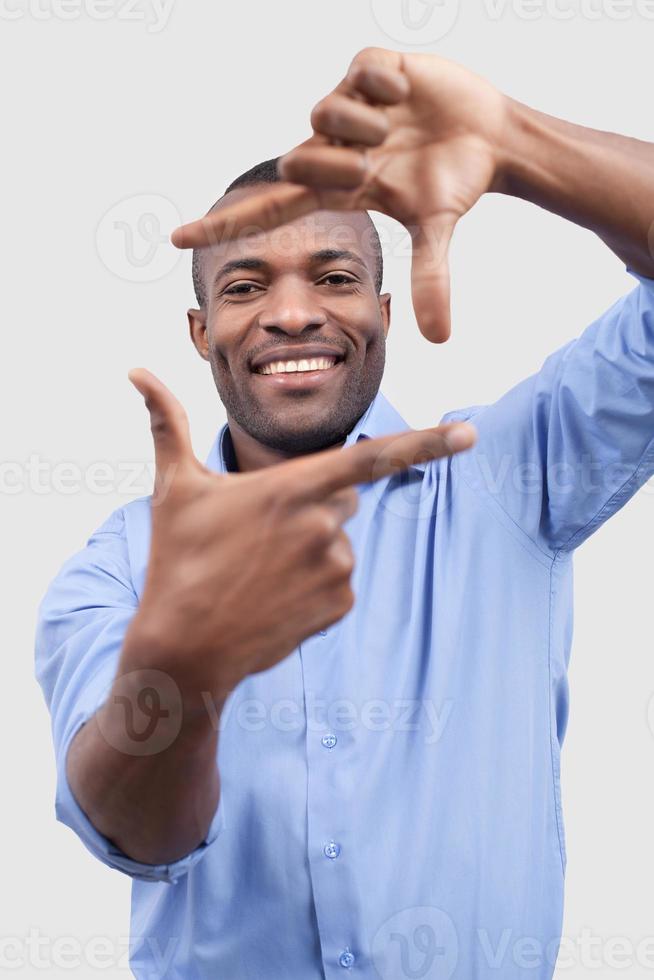 Focusing on you. Handsome young African man focusing on you and smiling while standing isolated on grey background photo