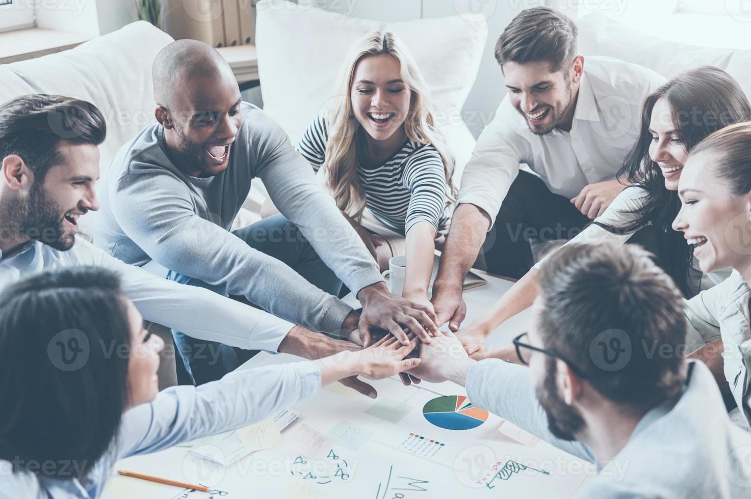 Together we are stronger Group of happy business people holding hands together while sitting around the desk photo