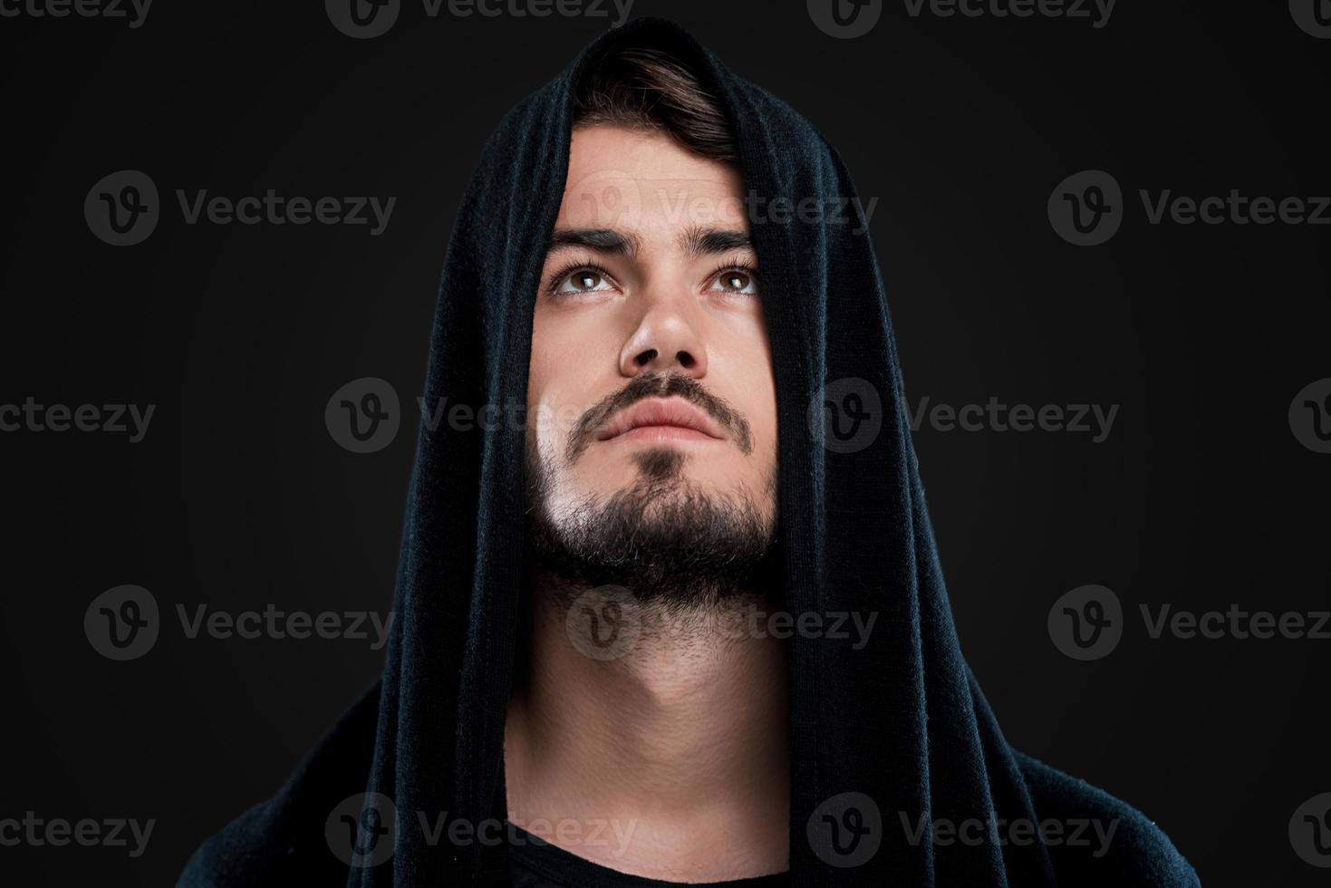 hombre misterioso. un joven apuesto con capucha negra mirando hacia arriba mientras se enfrenta a un fondo negro foto