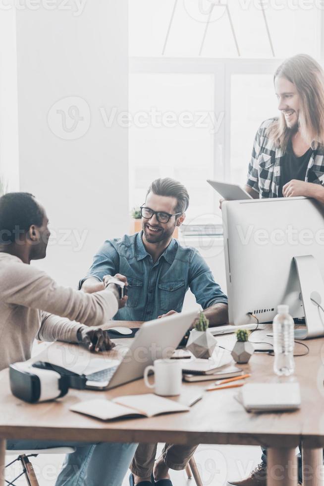 Beginning of a new partnership. Group of young business people working together in office while two men shaking hands and smiling photo