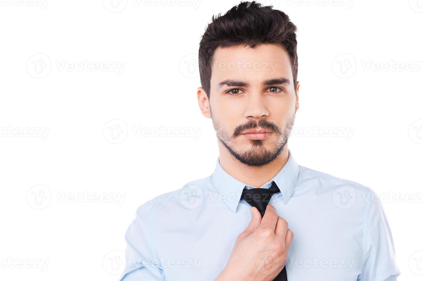Confident and successful. Confident young man in shirt and tie looking at camera and adjusting his necktie while standing against white background photo
