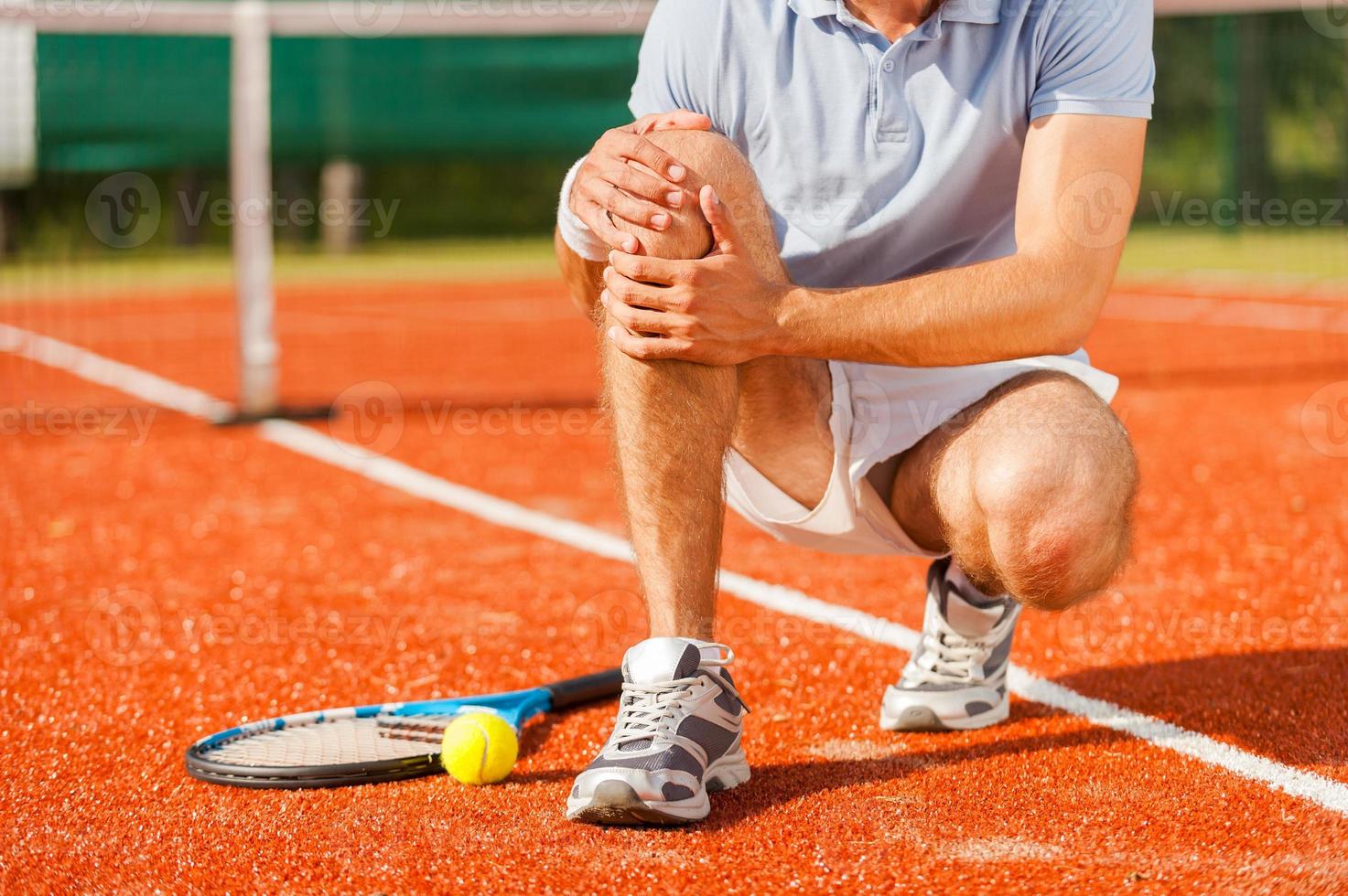 Sports injury. Close-up of tennis player touching his knee while sitting on the tennis court photo