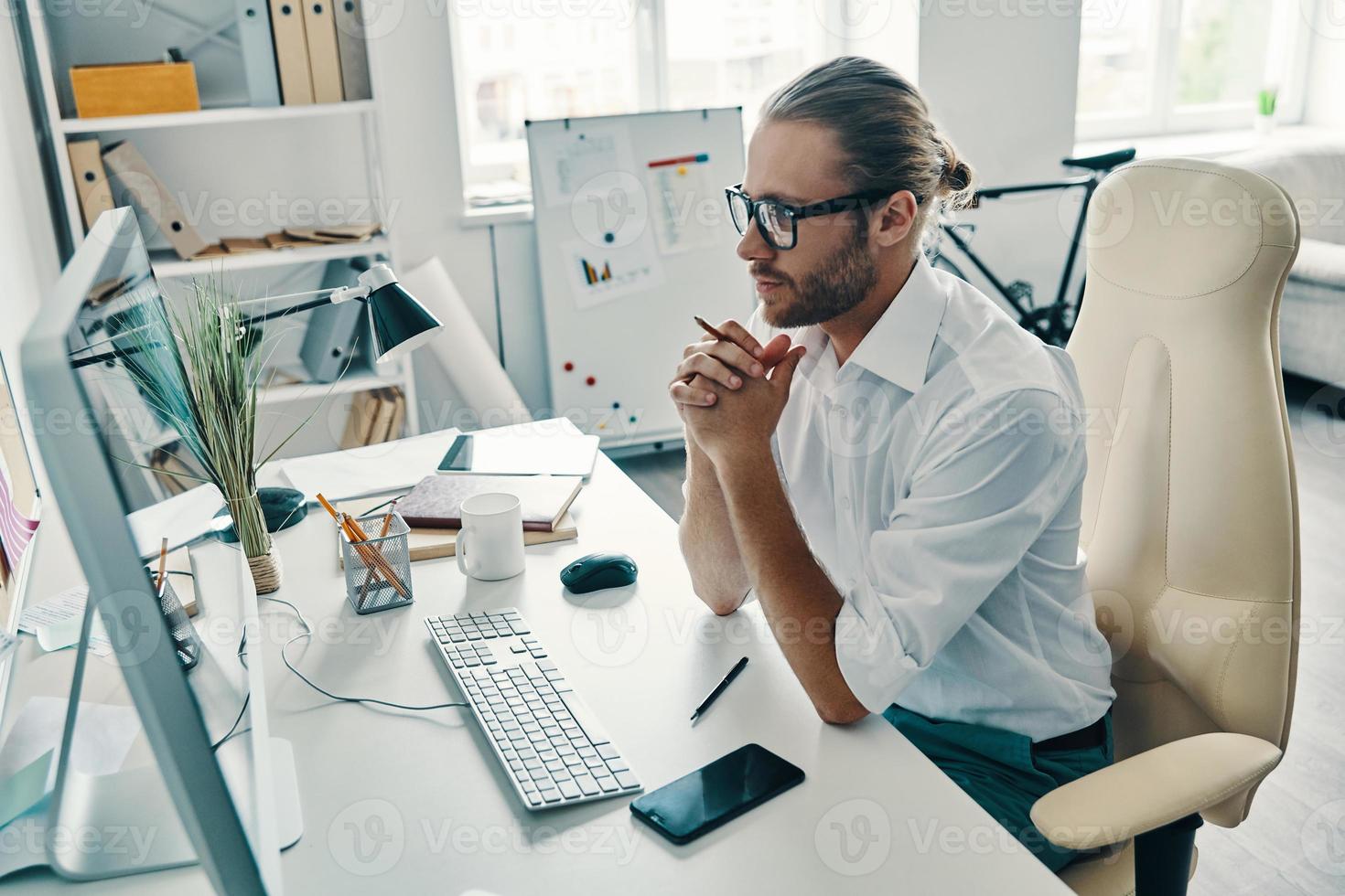 Concidering next step. Top view of thoughtful young man in shirt working using computer while sitting in the office photo