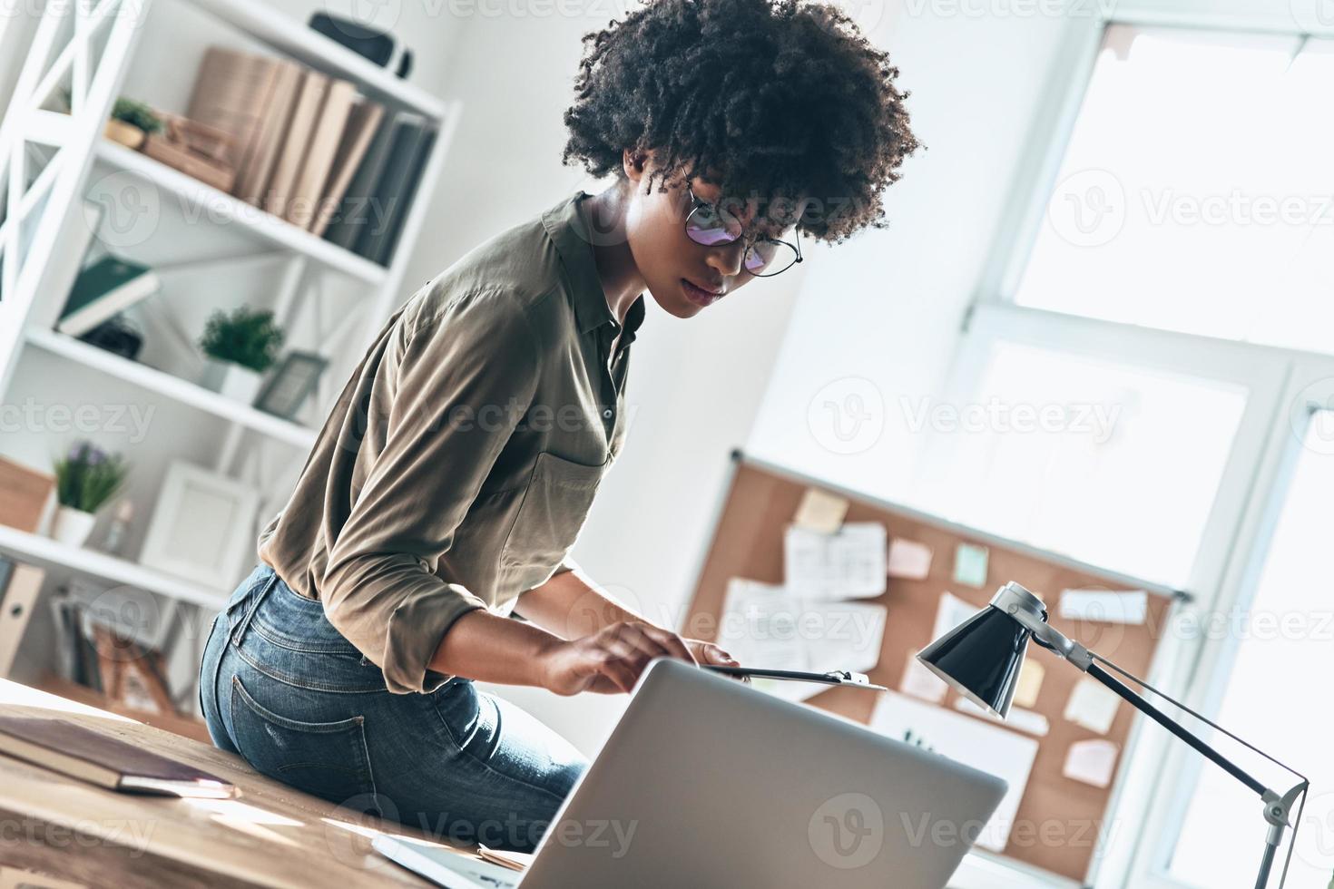 Paying attention to every detail. Thoughtful young African woman writing something down while working in the office photo