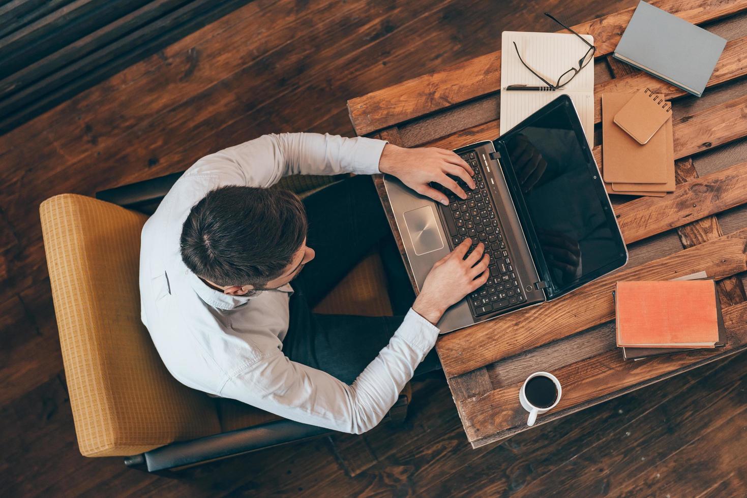 Casual business day. Top view of young man working on laptop while sitting at his working place photo