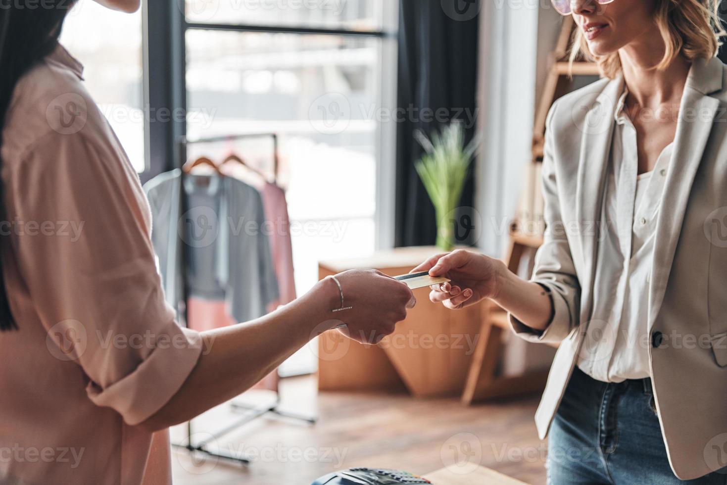 comprando y vendiendo. Cerca de una joven que le da una tarjeta de crédito a un vendedor mientras compra en la boutique de moda foto