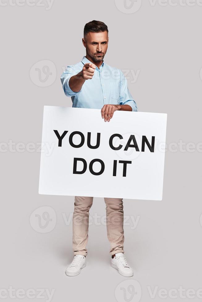 Never give up Full length of handsome young man holding poster and gesturing while standing against grey background photo