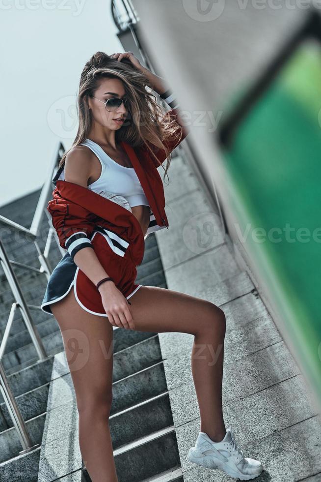 Sporty beauty. Attractive young woman in sport clothing keeping hand in hair while posing outdoors photo