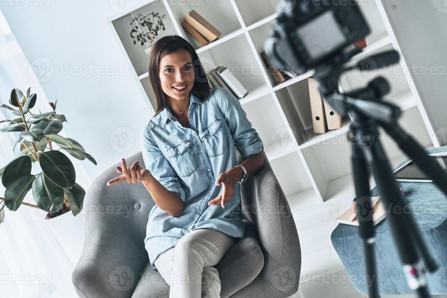 dando buenos consejos. atractiva mujer joven gesticulando y sonriendo mientras hace un nuevo video en el interior foto