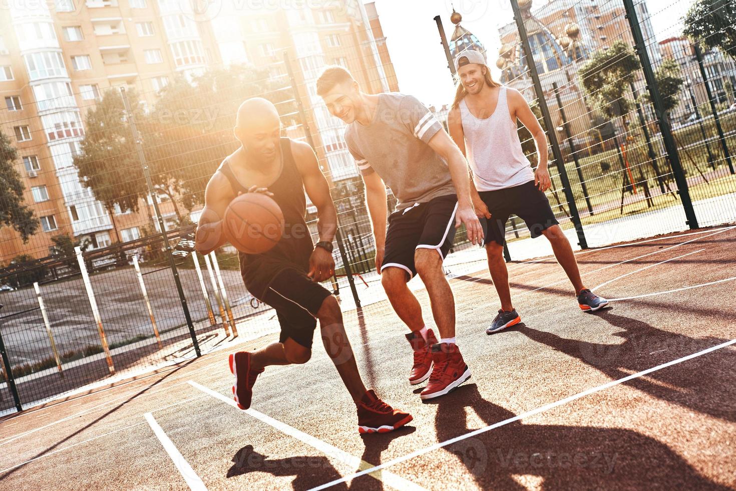 verdadero ganador grupo de jóvenes vestidos con ropa deportiva jugando baloncesto y sonriendo mientras pasan tiempo al aire libre foto