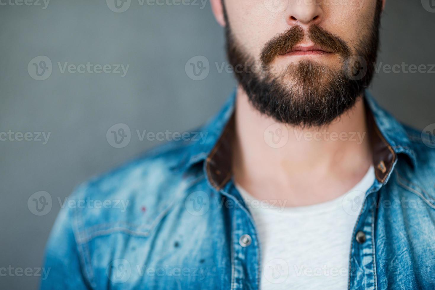 Beard is his style. Cropped image of young man wearing shirt while standing against grey background photo