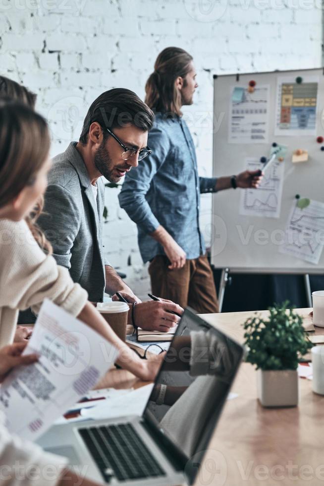 Sharing ideas. Modern young man pointing at flipchart while conducting a presentation in the board room photo