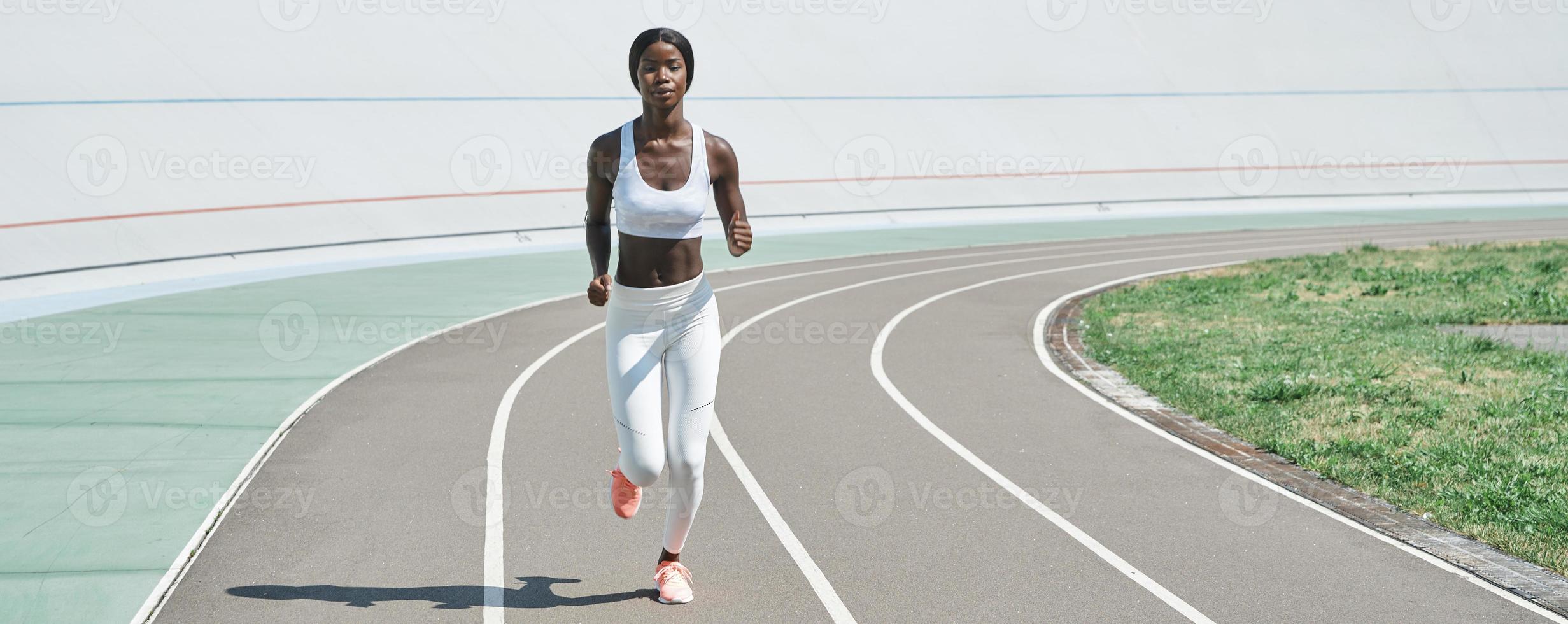 toda la longitud de una hermosa joven africana vestida con ropa deportiva corriendo en la pista al aire libre foto