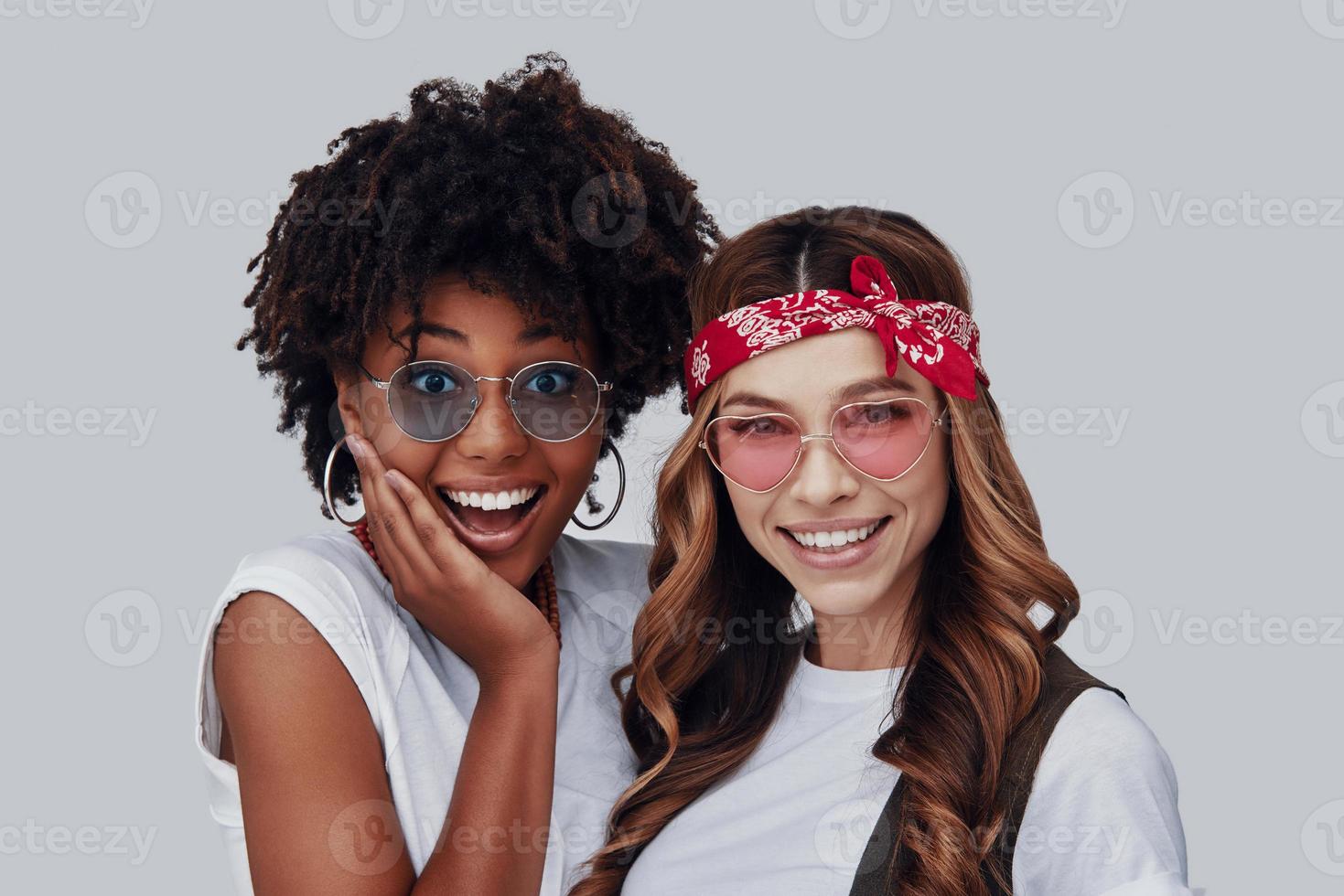 Two attractive young women looking at camera and smiling while standing against grey background photo