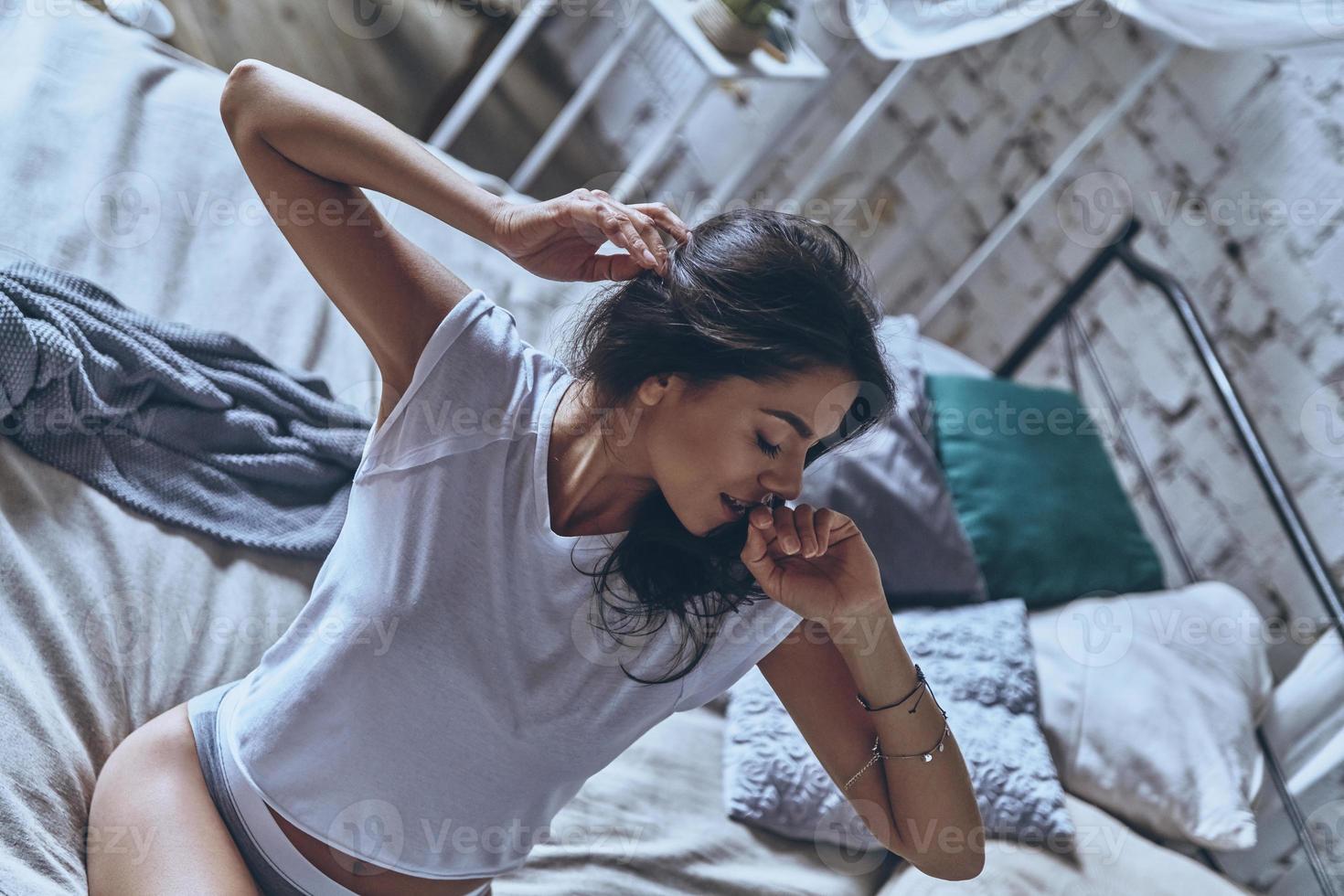 Waking up to a beautiful day. Top view of attractive young woman stretching and smiling while sitting on the bed at home photo