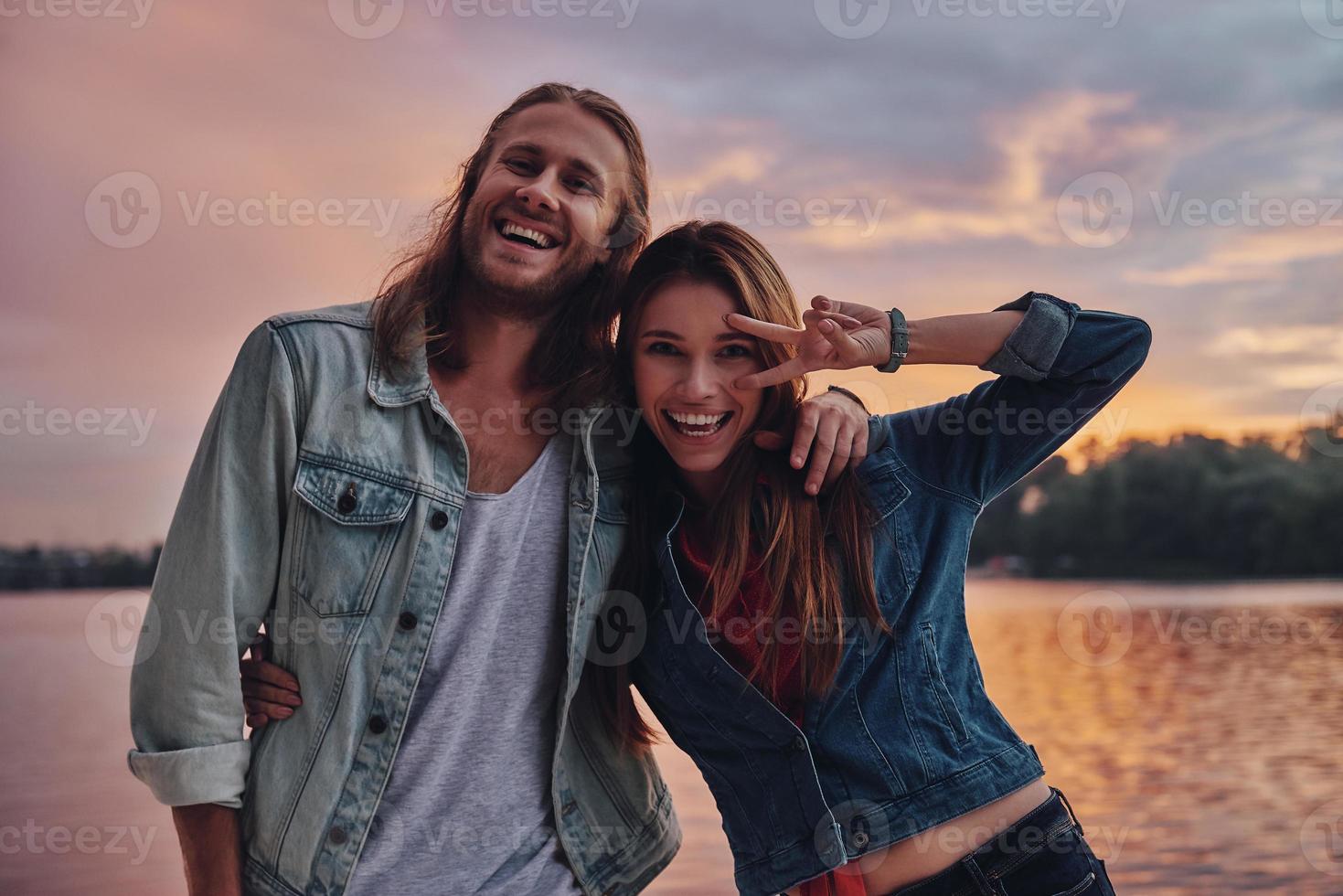 Playful couple. Happy young couple in casual wear smiling and looking at camera while standing near the lake photo