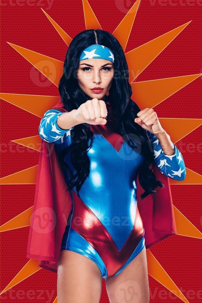 Are you ready to fight Beautiful young woman in superhero costume looking at camera while standing in fighting stance against red background photo