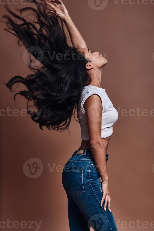 Strong hair. Beautiful young woman touching her hair while standing against brown background photo