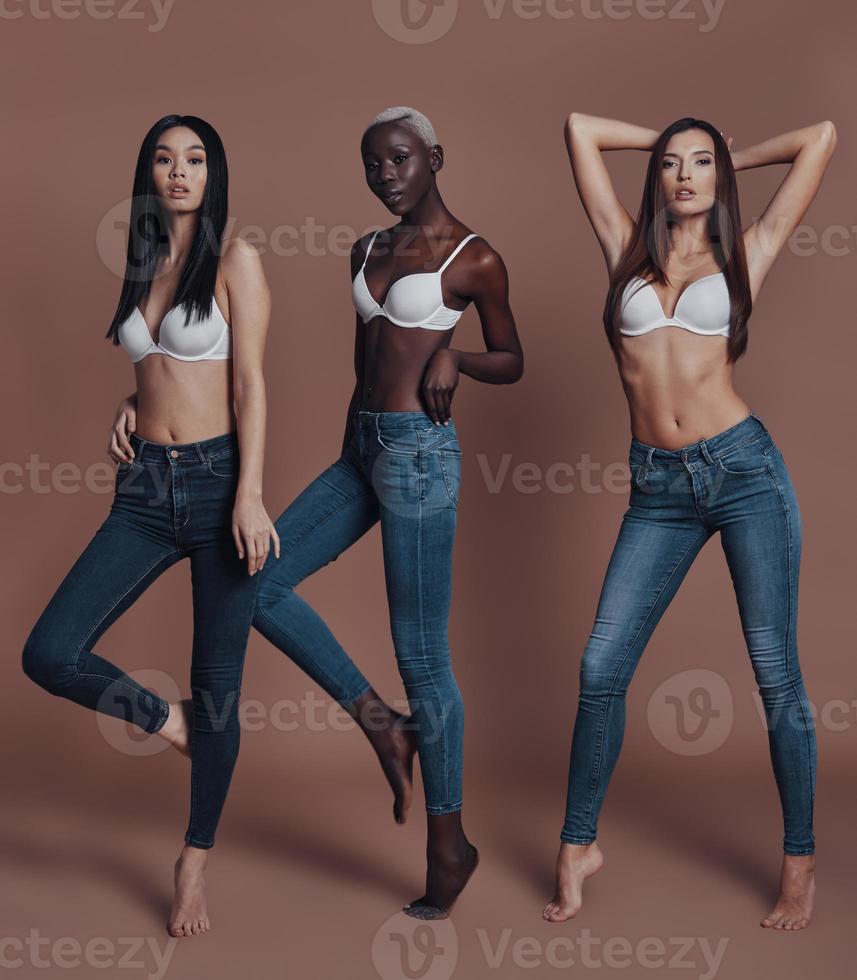 Full of life energy. Full length of three attractive young women looking at camera while standing against brown background photo