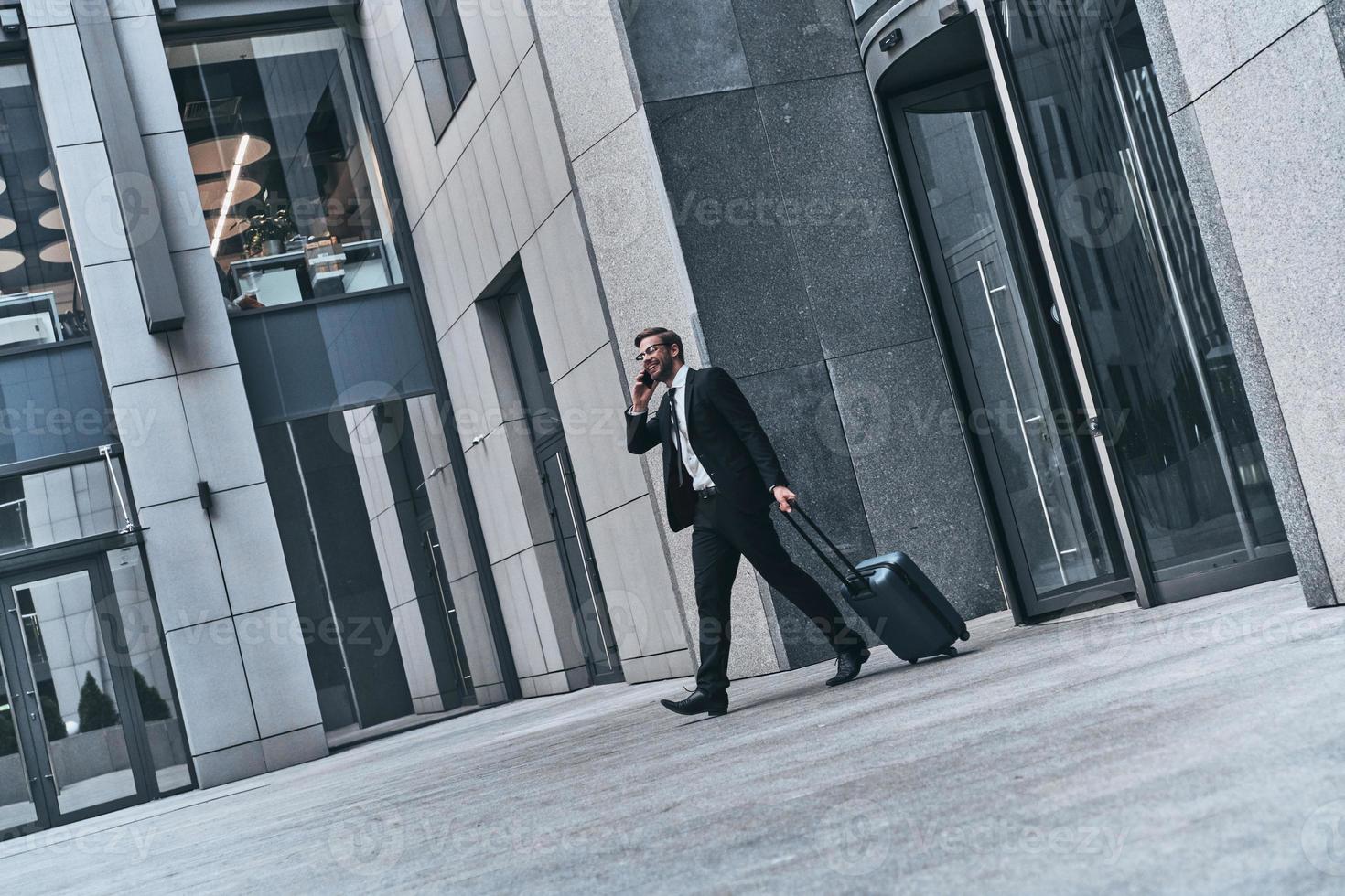 Quick business talk. Full length of young man in full suit talking on the phone and smiling while walking outdoors photo