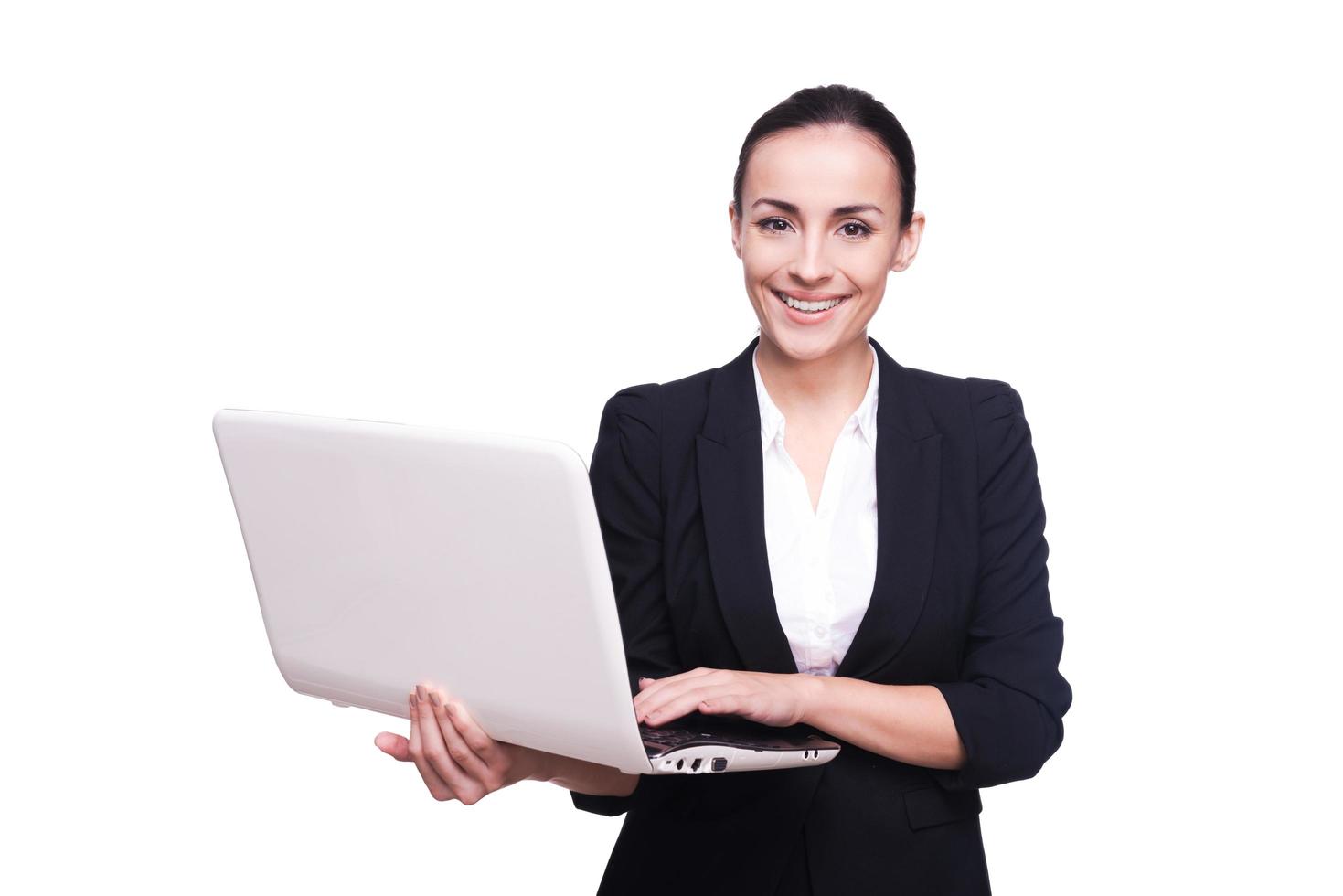 Confident in her laptop. Beautiful young woman in formalwear working on laptop isolated on white background photo