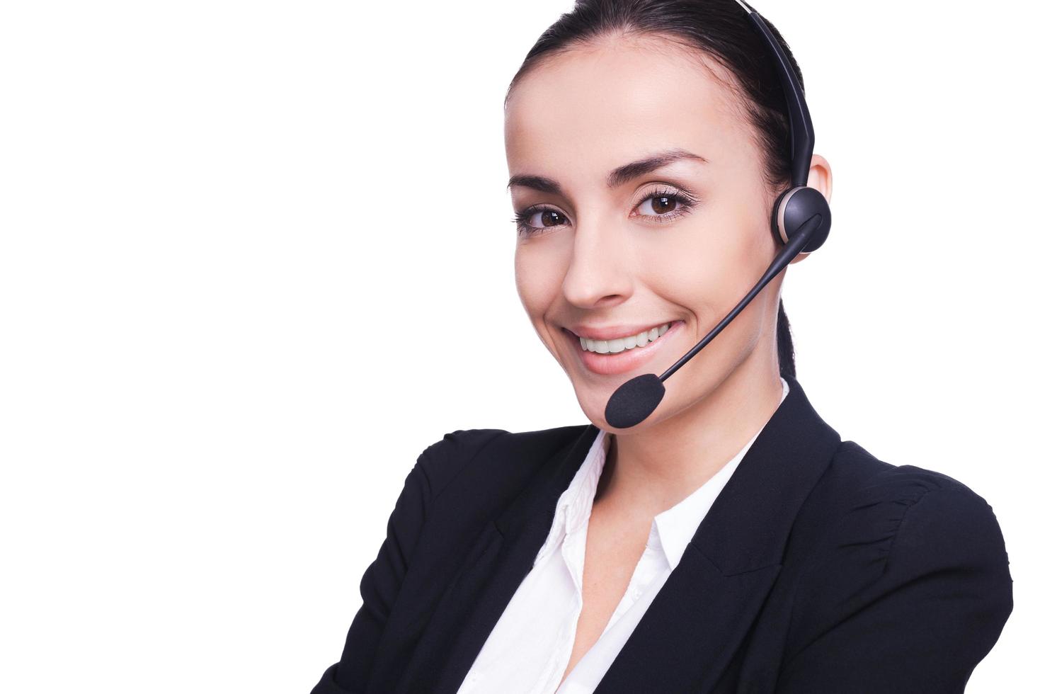 hermosa operadora femenina. mujer joven segura de sí misma con auriculares sonriendo y manteniendo los brazos cruzados mientras está aislada en blanco foto