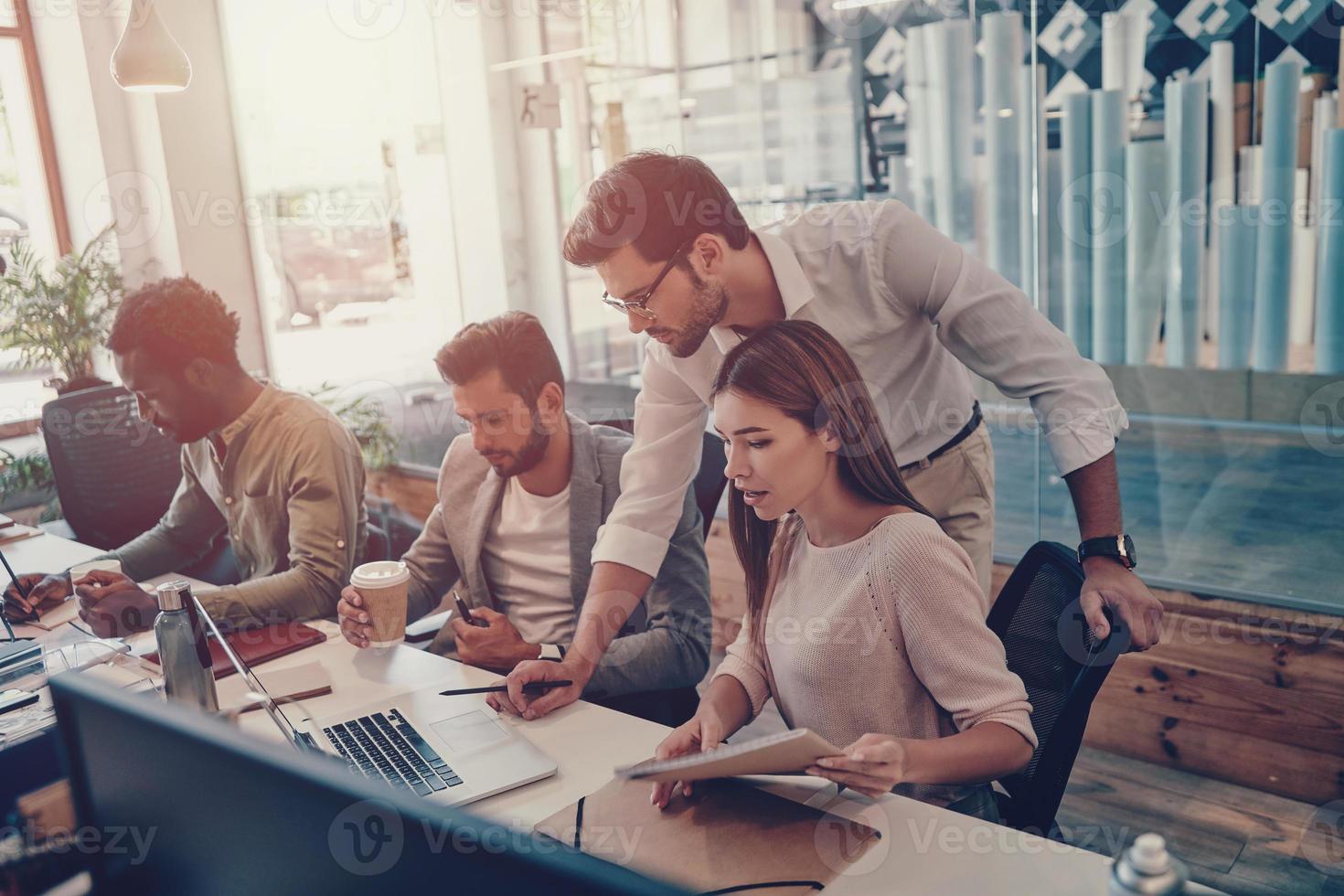 Group of young modern people in smart casual wear communicating and using modern technologies while working in the office photo
