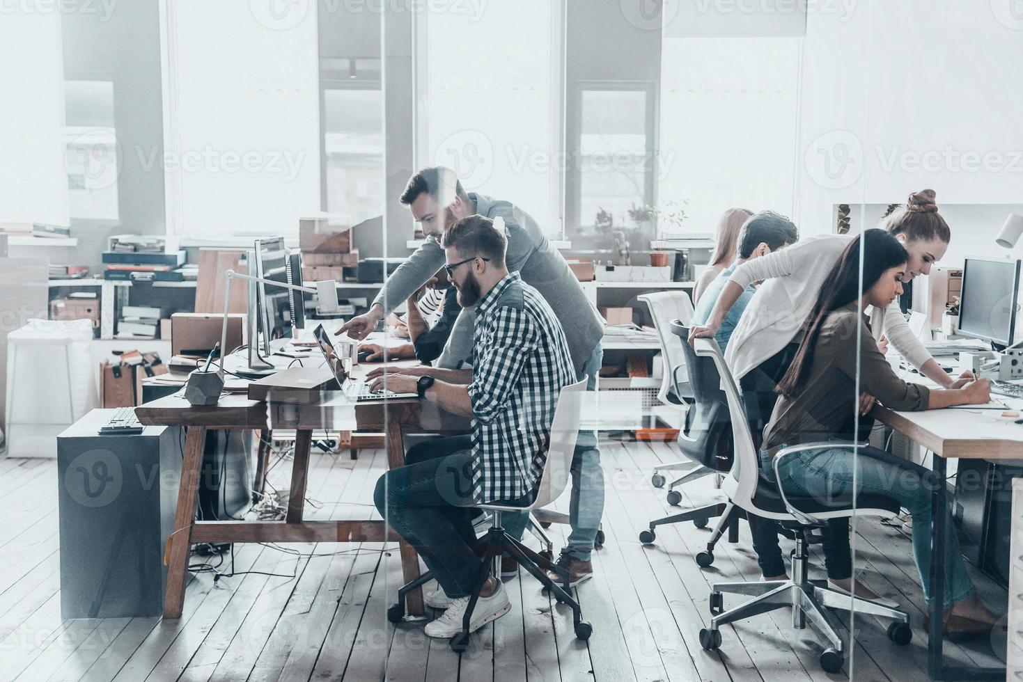 discutiendo temas de negocios. grupo de jóvenes empresarios sentados en el escritorio de la oficina y discutiendo algo mientras trabajan juntos detrás de la pared de vidrio en la oficina creativa foto