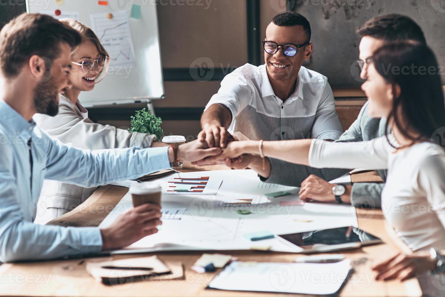 Successful team. Young modern people in smart casual wear holding hands on top of one another in a symbol of unity while working in the creative office photo