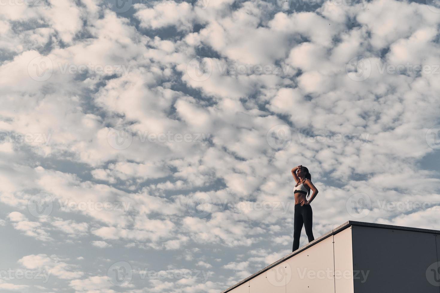 Workout is over. Modern young woman in sports clothing relaxing while standing on the roof outdoors photo