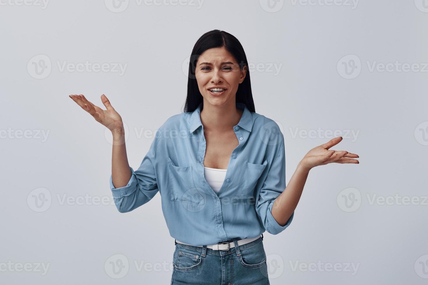 mujer joven atractiva haciendo una cara y gesticulando mientras está de pie contra el fondo gris foto