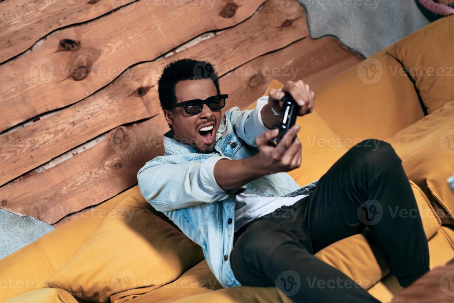 In it to win. Modern young man in casual clothing playing video games and making a face while spending time at home photo