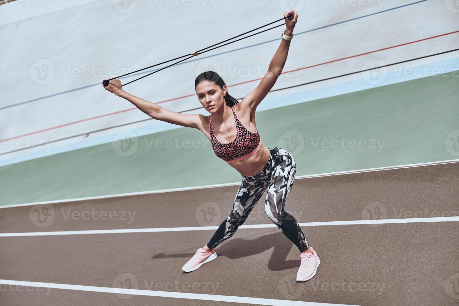 decidido a ganar. Hermosa mujer joven en ropa deportiva haciendo ejercicio  con banda de resistencia mientras está de pie en la pista de atletismo al  aire libre 13526959 Foto de stock en