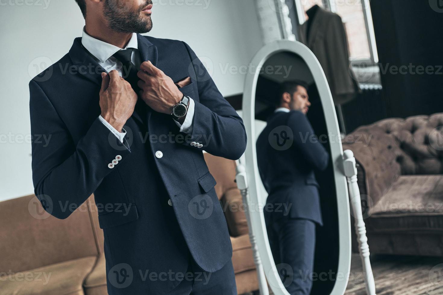Everything must be perfect. Close up of young man in full suit adjusting jacket while standing indoors photo