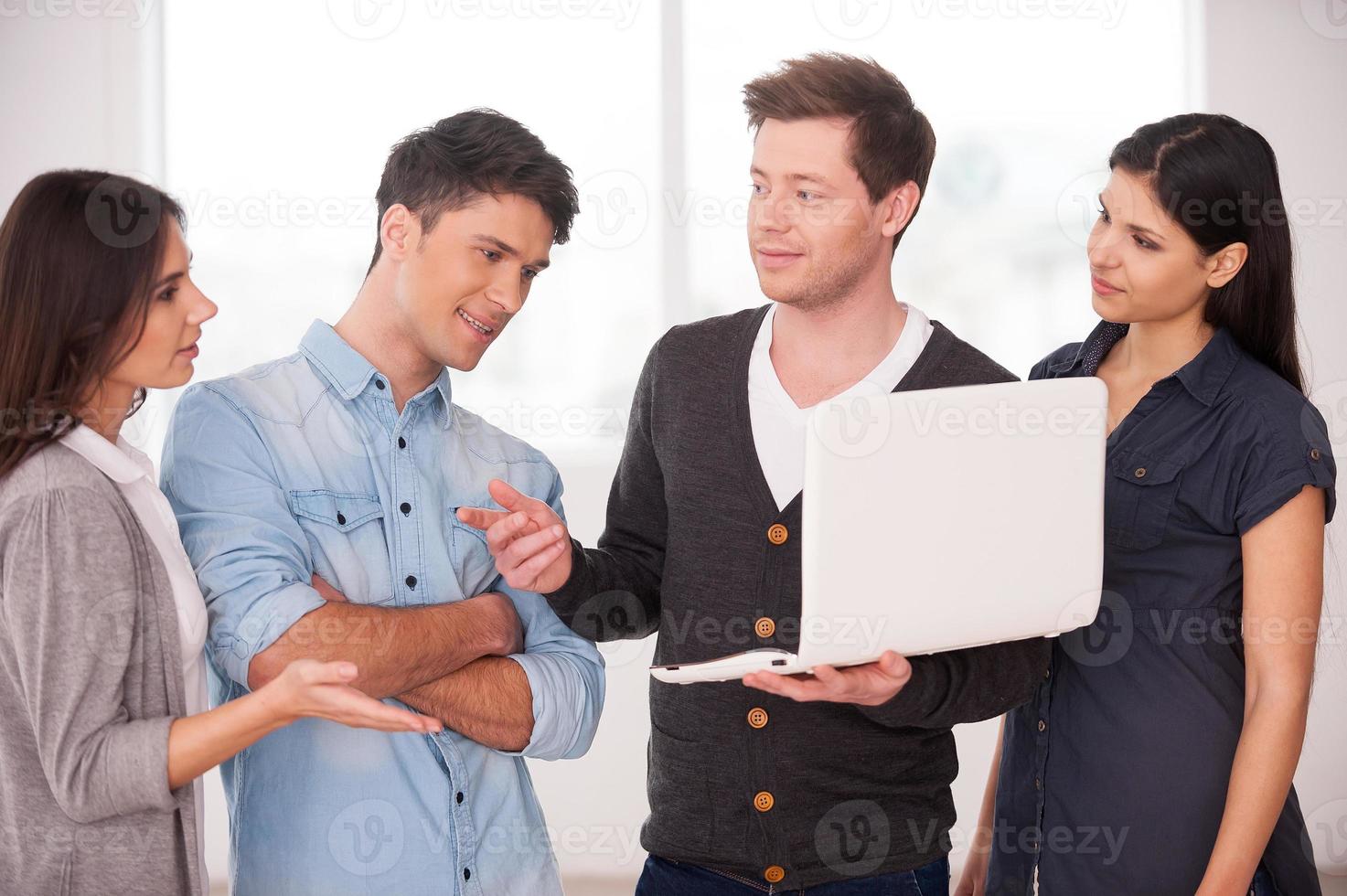 Discussing project together. Group of young people discussing something while one man holding laptop photo