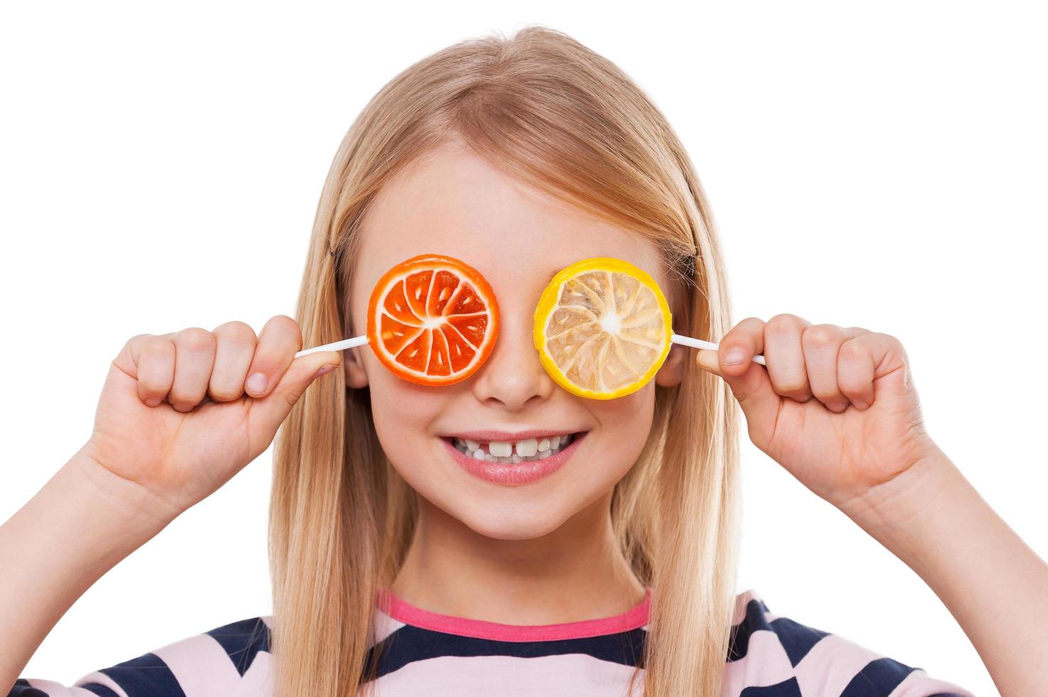 Having fun with candies. Cheerful little girl covering eyes with lollipops and smiling while isolated on white photo