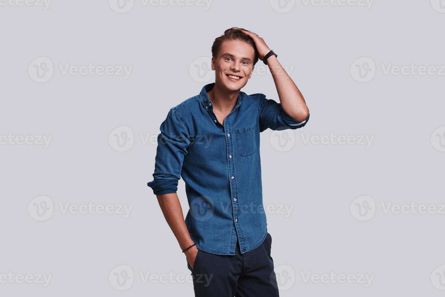 Cheerful and handsome. Handsome young man looking at camera and smiling while standing against grey background photo