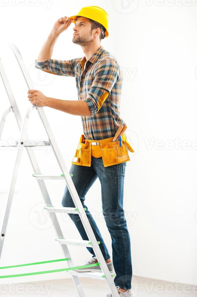 Climbing to the top. Concentrated young repairman climbing up the ladder and adjusting his hardhat photo