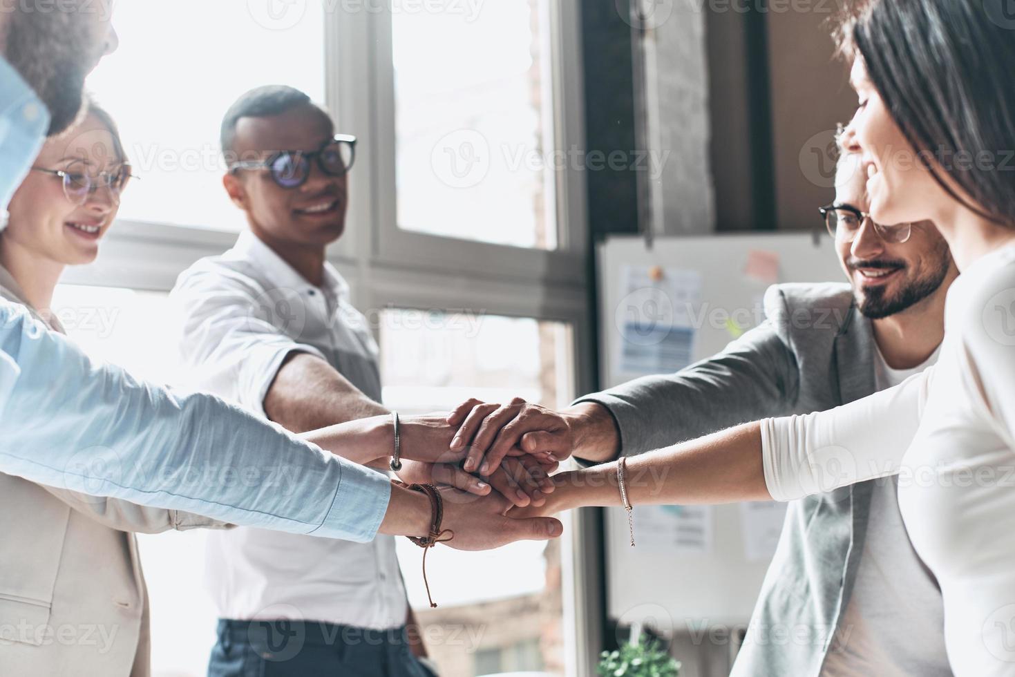 To success Young modern people in smart casual wear holding hands on top of one another in a symbol of unity while working in the creative office photo