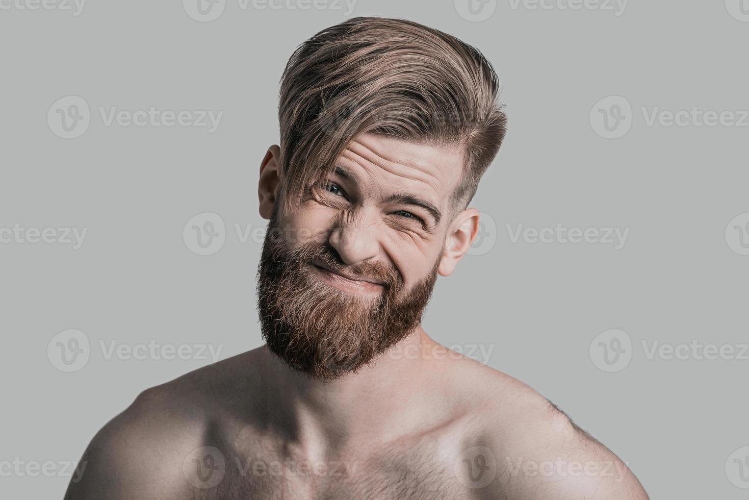 Portrait of young handsome man making face and looking at camera while being in front of grey background photo