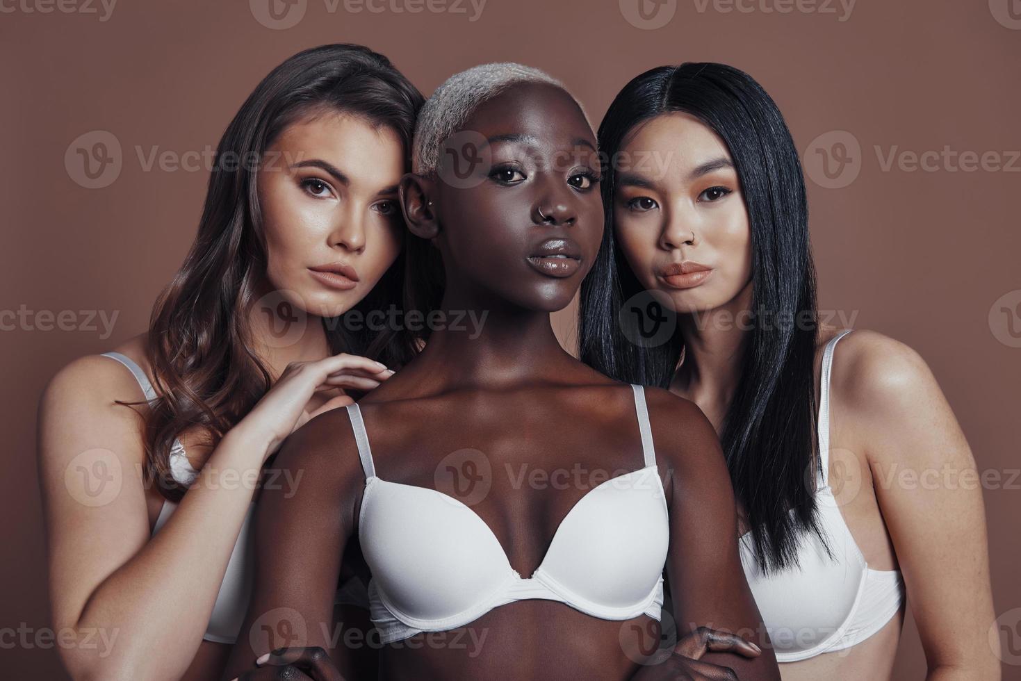 Irresistible girls. Three attractive young women looking at camera while standing against brown background photo