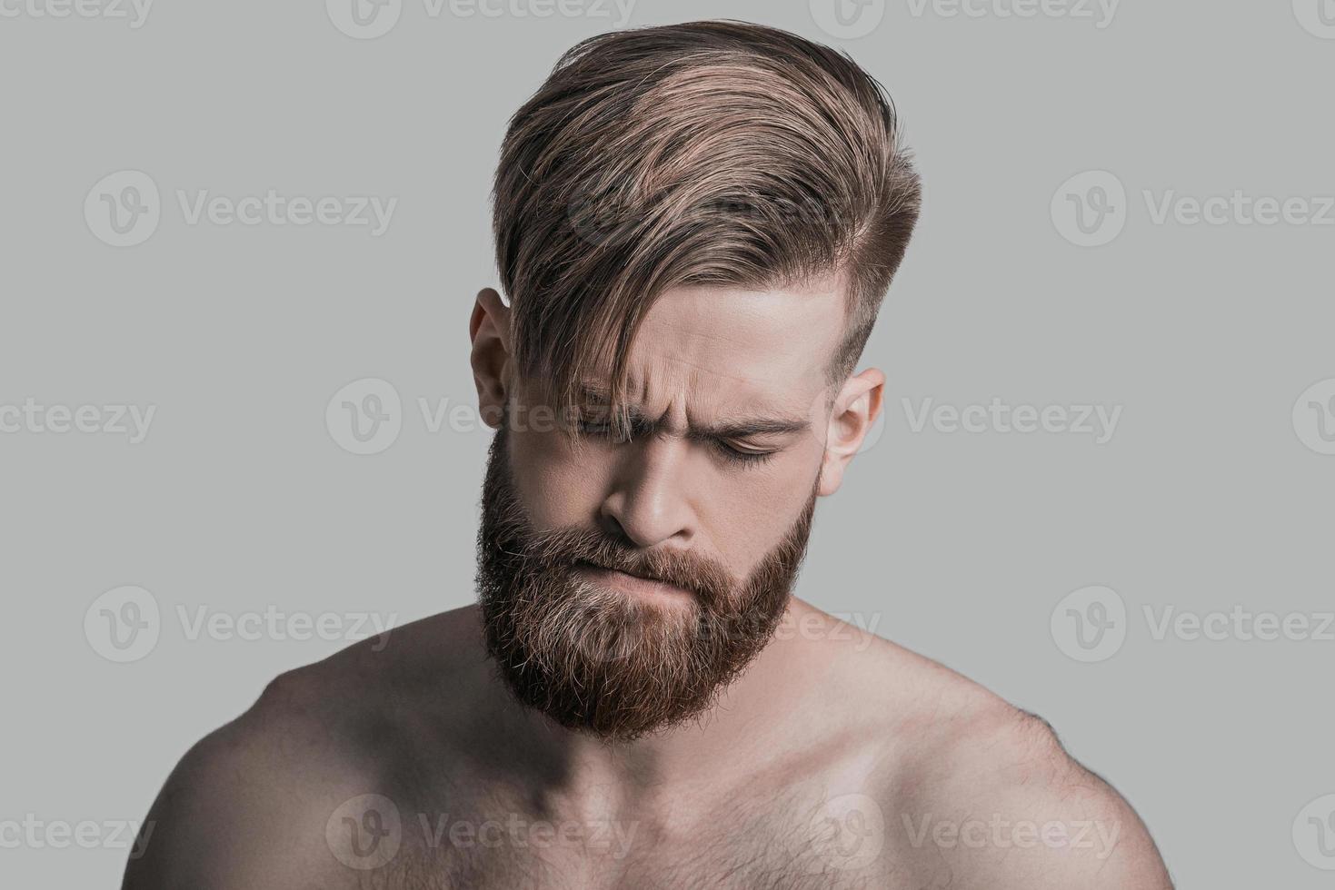 Upset about something. Portrait of young man keeping eyes closed while being in front of grey background photo