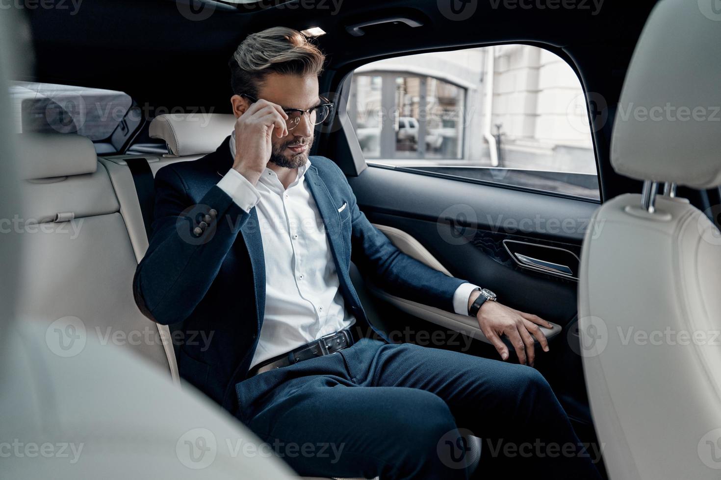 Confident manager. Handsome young man in full suit adjusting his eyewear while sitting in the car photo