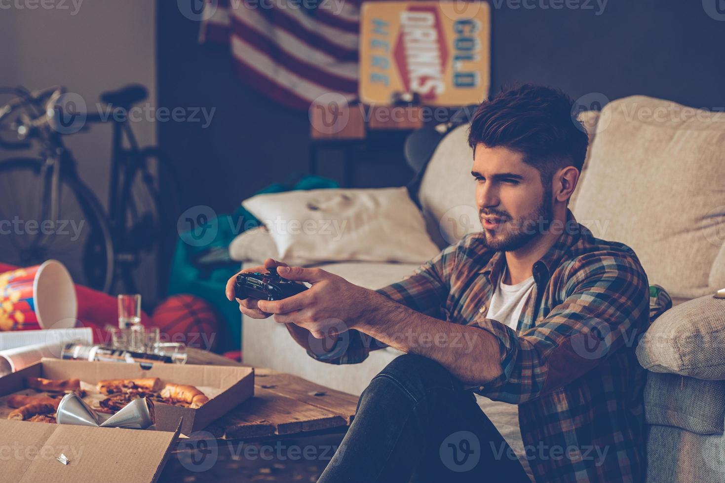 Exhausted gamer. Frustrated young man holding joystick while sitting on the floor in messy room after party photo